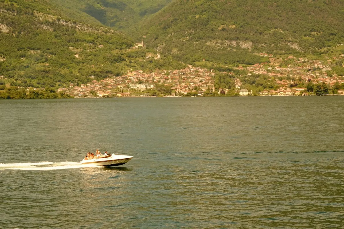 Petit bateau de plaisance naviguant devant un village au bord d'un lac
