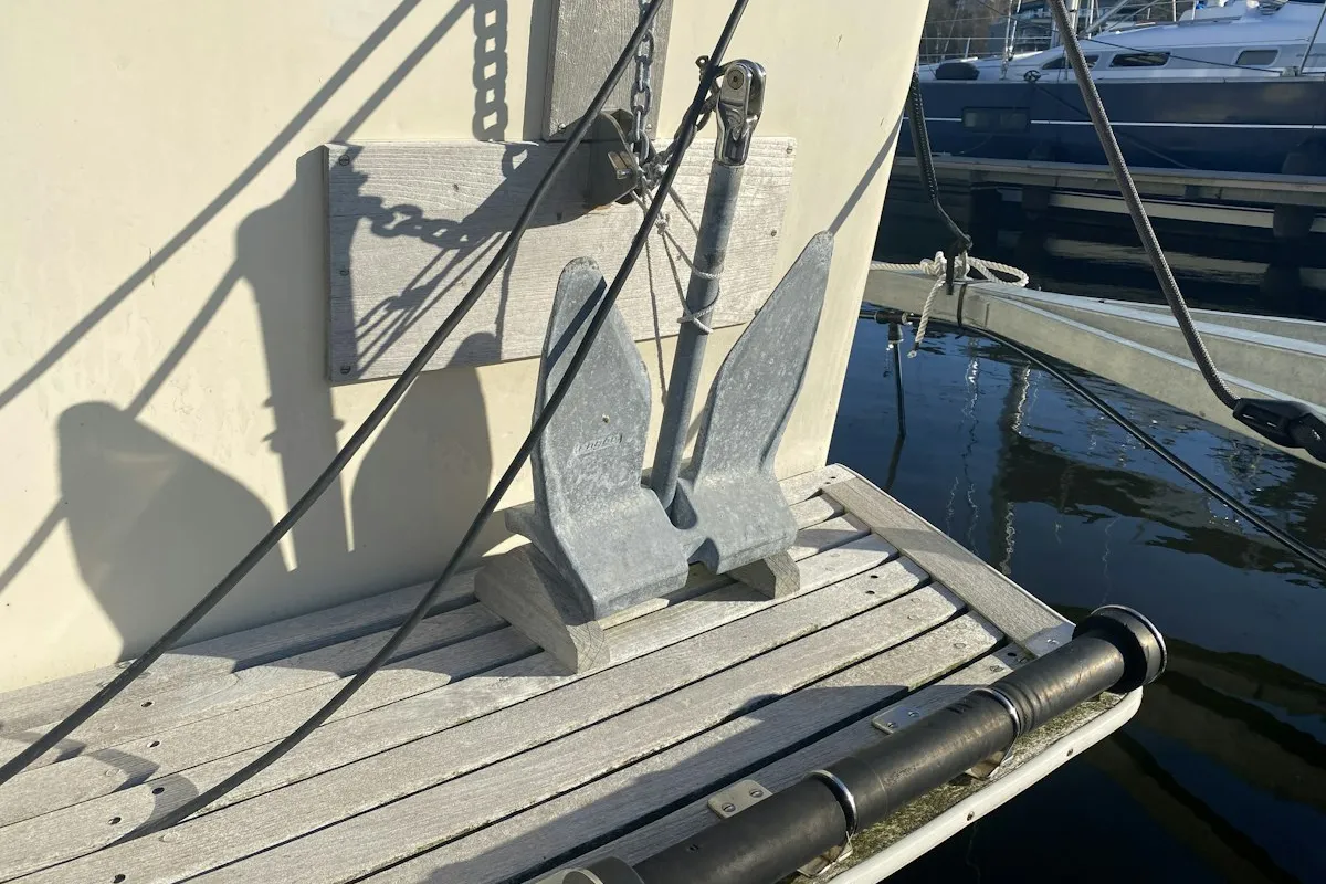 Ancre moderne posée sur un ponton, coque d'un bateau à l'arrière-plan