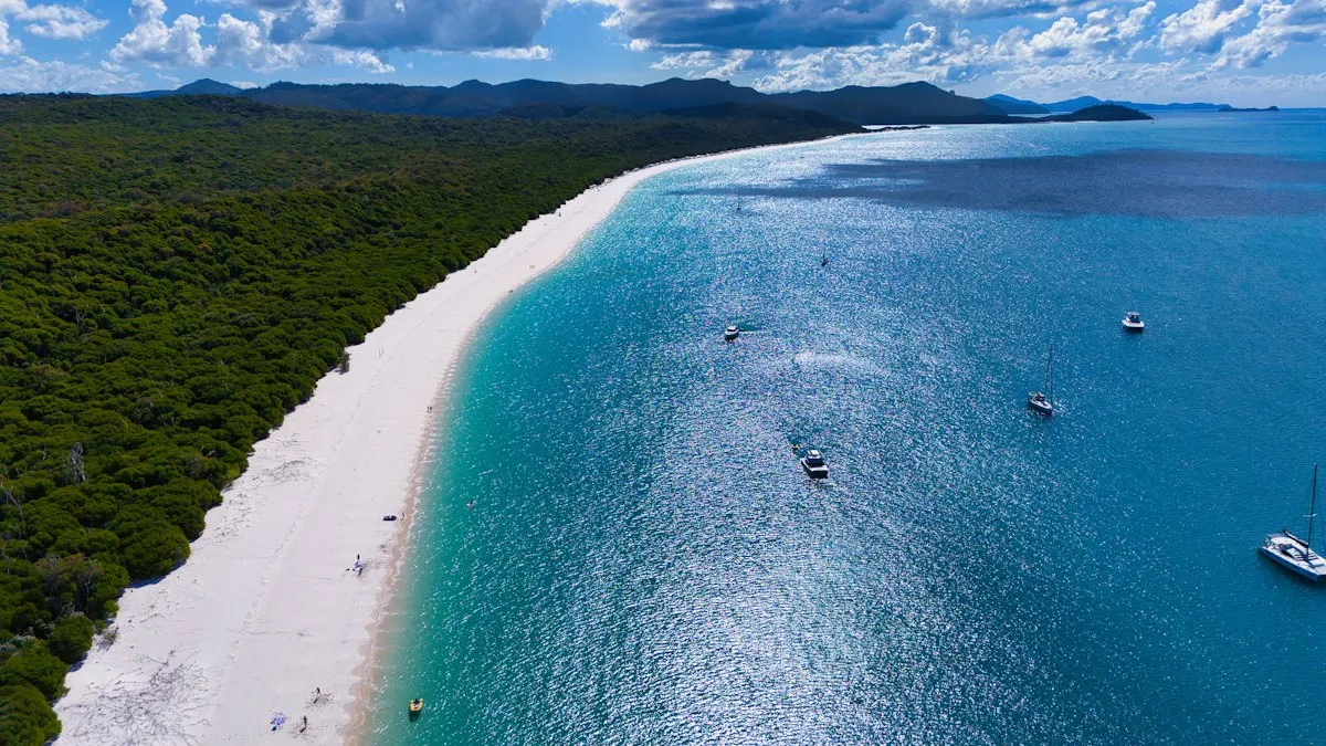 Plage de sable blanc et eau turquoise avec voiliers au mouillage