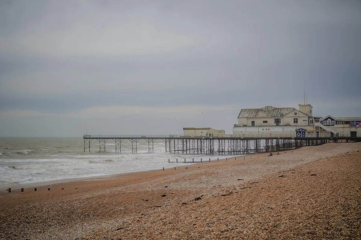 Plage de galets et jetée sous un ciel gris de la Manche